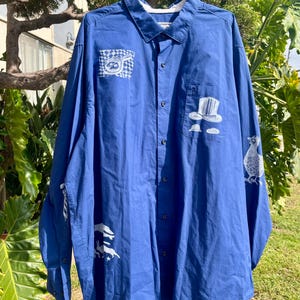 May include: A blue long-sleeved button-down shirt with white graphic designs. The designs include a bird, a hat, and a geometric pattern.