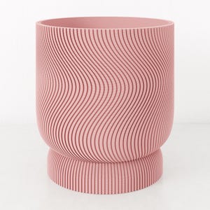 Può includere: Un vaso rosa, cilindrico, con un design ondulato e scanalato. Il vaso ha una base arrotondata e un'ampia apertura. Il colore è un rosa tenue e polveroso. Le scanalature verticali creano una superficie strutturata.