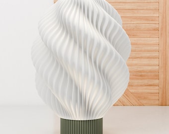 May include: A white ceramic table lamp with a wavy, organic design. The lamp has a green base and a white shade.