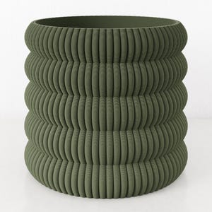 May include: A large, olive green planter with a ribbed, stacked design. The cylindrical pot has a wide opening and a series of rounded, horizontal bands that create a textured surface. The planter is suitable for indoor or outdoor use.