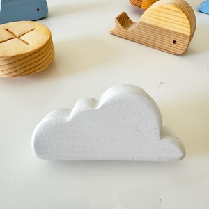 Puede incluir: Un adorno de madera blanco en forma de nube. La nube es lisa y tiene una forma ligeramente redondeada.