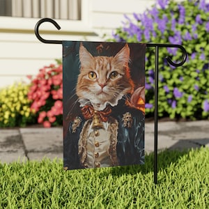 May include: A garden flag featuring a portrait of a ginger cat dressed in a blue and gold costume with a bell around its neck. The cat has a serious expression and is looking directly at the viewer. The background is a dark, blurry forest scene.