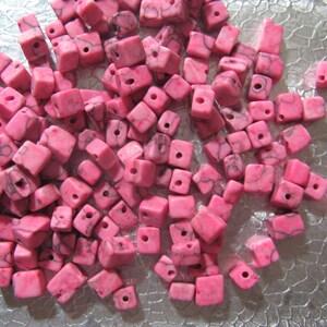 May include: A pile of pink and white marble cube beads with a hole drilled through the center of each bead.