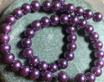 May include: Strands of dark purple, round beads with a pearlescent finish. The beads are strung together, creating a necklace or bracelet. The beads are approximately 8mm in diameter.