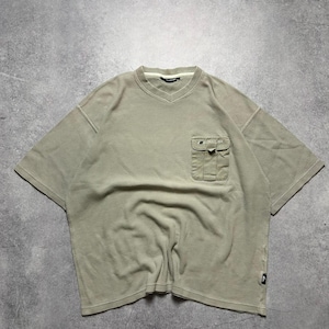 May include: A light green short-sleeved shirt with a V-neck and a pocket on the chest. The shirt has a textured waffle-knit design and a small logo near the hem. The shirt is made of a soft, comfortable material.