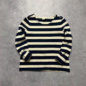 May include: A long-sleeved shirt with horizontal navy blue and cream stripes. The shirt has a boat neck and two buttons on the shoulder. The sleeves end at the wrist. The shirt is made of a soft material.