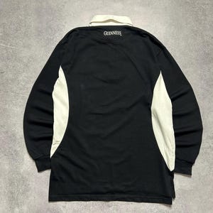 Puede incluir: Camiseta de rugby negra de manga larga con cuello y paneles laterales blancos. La palabra "GUINNESS" est&aacute; impresa en blanco en la parte posterior del cuello. Dise&ntilde;o cl&aacute;sico.