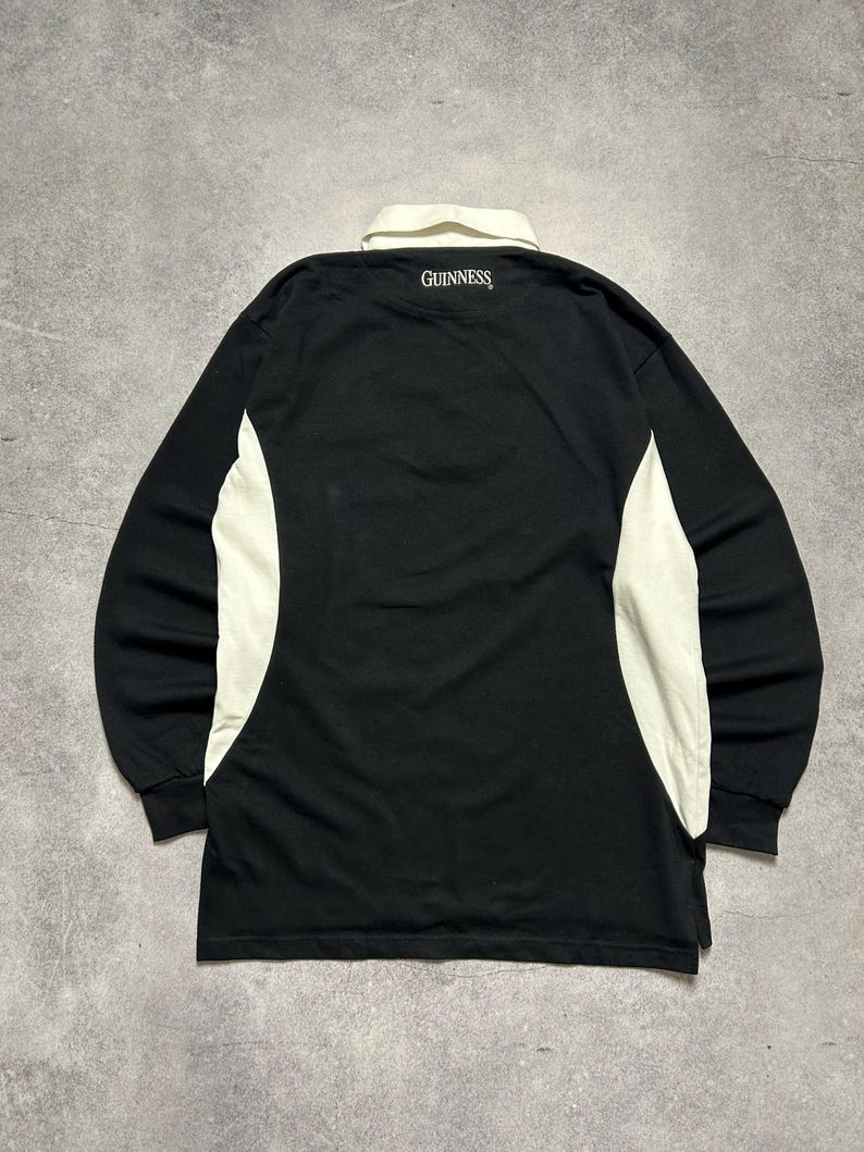 Puede incluir: Camiseta de rugby negra de manga larga con cuello y paneles laterales blancos. La palabra "GUINNESS" est&aacute; impresa en blanco en la parte posterior del cuello. Dise&ntilde;o cl&aacute;sico.