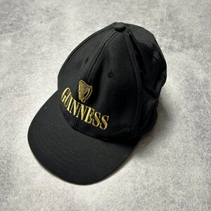 Pu&ograve; includere: Cappellino da baseball nero con il logo Guinness ricamato in oro. Il cappellino ha una visiera curva e un bottone sulla parte superiore. Il logo Guinness presenta un'arpa e il nome del marchio.