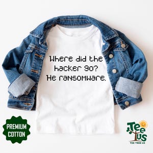 May include: White t-shirt with the text "Where did the hacker go? He ransomware." The shirt is under a blue denim jacket. The shirt has a green "Premium Cotton" label and a "Tee Tree Us" logo.