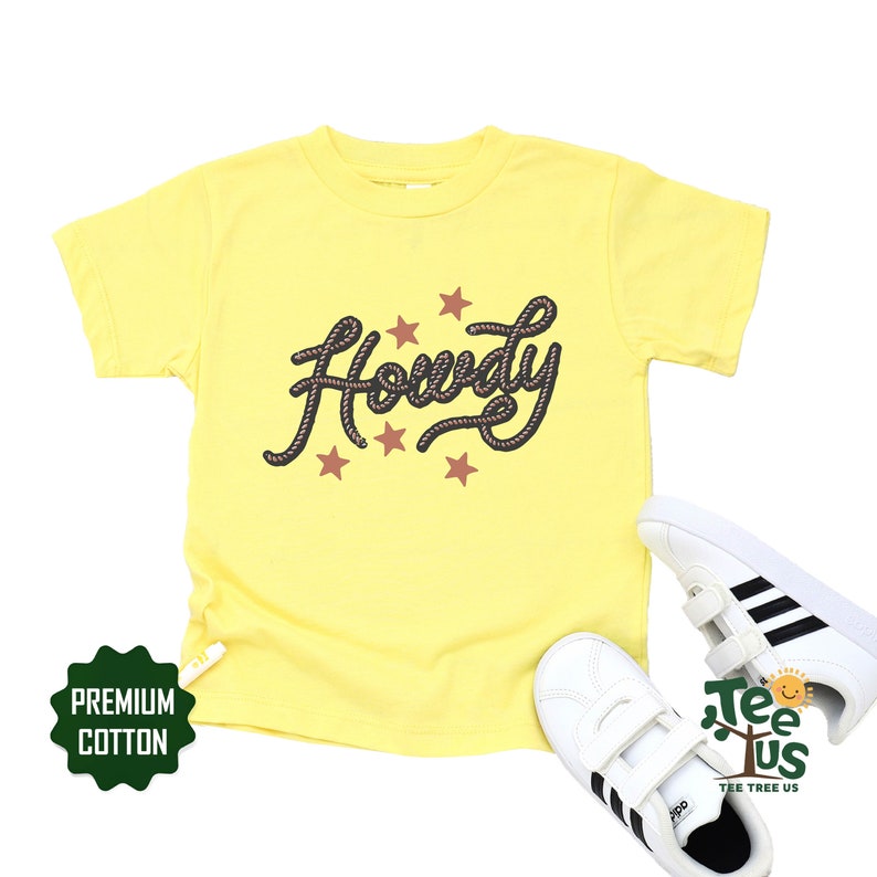 May include: Yellow short-sleeved t-shirt with the word "Howdy" in a rope-like font and five red stars. The shirt is made of premium cotton.