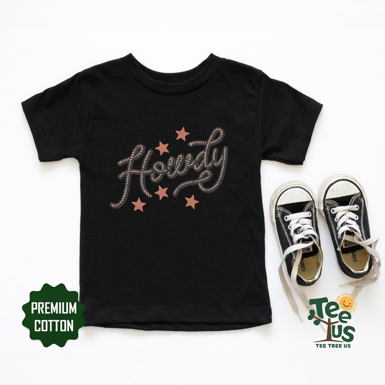 May include: Black t-shirt with the word "Howdy" written in a rope-like font with five brown stars. The shirt is made of premium cotton.
