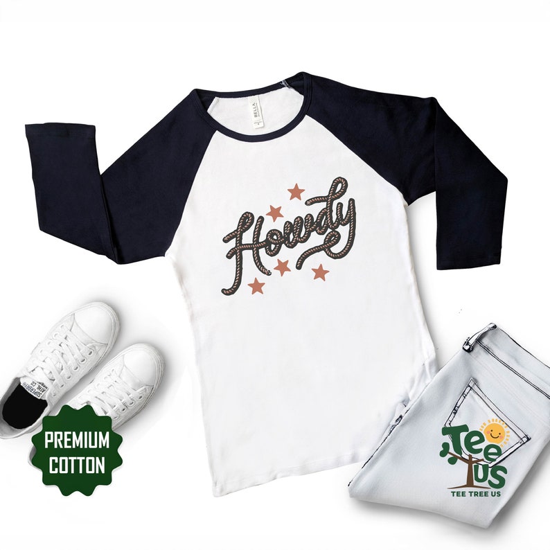May include: White and navy blue baseball tee shirt with a rope design that says "Howdy" in a cursive font. The shirt has five brown stars around the text.