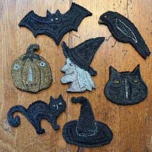 May include: A set of seven Halloween-themed felt ornaments. The ornaments include a black bat, a black cat, a black witch's hat, a black witch, a black crow, a pumpkin, and a black cat's face.