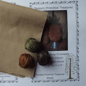 May include: A craft project setup featuring a tan fabric, three spools of thread in shades of green, brown, and tan, and a printed pattern with a pineapple design. The pattern is labeled "Teresa's Primitive Treasures."