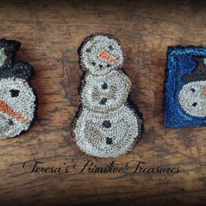 May include: Three handmade felt snowman ornaments. One snowman is white with a black hat and a red berry on top. The second snowman is white with a black hat and a green holly sprig on top. The third snowman is white with a black hat and a blue background.