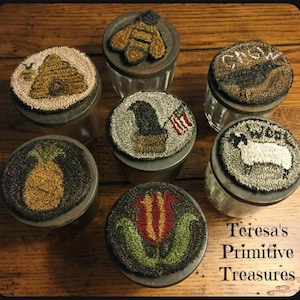 May include: Seven glass jars with lids decorated with various needlepoint designs. The designs include a beehive, a bird, a pineapple, a tulip, a sheep, a bird with an American flag, and a bird with the word "SNOW". The jars are on a wooden surface. The text "Teresa's Primitive Treasures" is visible at the bottom of the image.