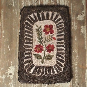 May include: A rectangular, handmade rug with a floral design. The rug features a central cream-coloured panel with red flowers and green foliage. The flowers are surrounded by a brown border with a scalloped edge, and a dark brown outer border.