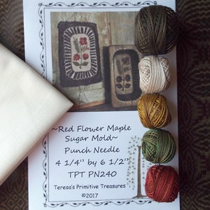 May include: A punch needle kit for a Red Flower Maple Sugar Mold design. The kit includes a piece of white fabric, six skeins of embroidery floss in various colors, and instructions. The design measures 4 1/4 inches by 6 1/2 inches.
