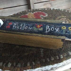 May include: A wooden box with a hinged lid, decorated with a hand-stitched design of flowers and the words "Button Box". The box is open and contains a collection of buttons.