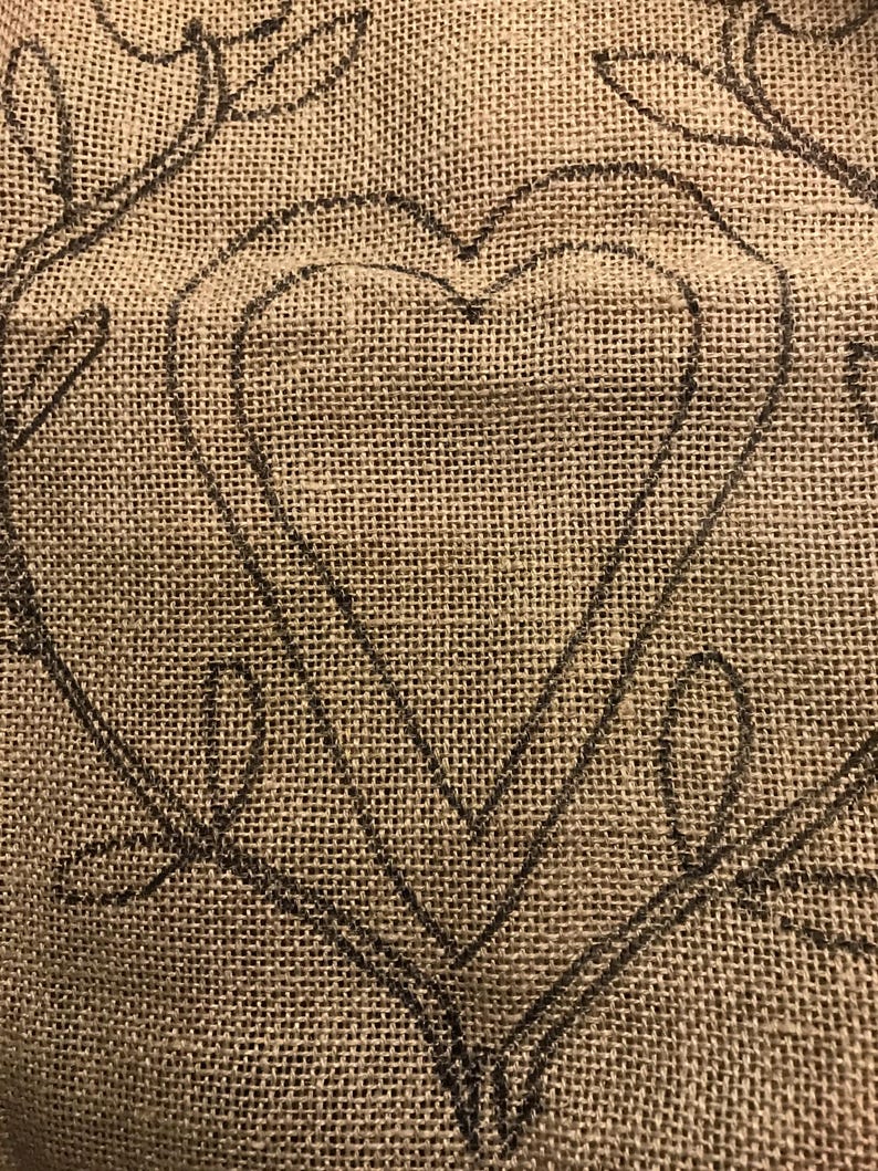 May include: A close-up of a burlap fabric with a black outline of a heart shape. The heart is double-layered, creating a three-dimensional effect.