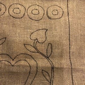 May include: A close-up of a burlap fabric with a black outline of a heart and a floral design. The fabric has the words "Winterheart" and "Mix" written on it.