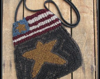 May include: Handmade, textured shoulder bag featuring a patriotic design. The bag showcases a flag motif with red and white stripes, a blue field with stars, and a large gold star. The bag has a dark gray background and a matching strap.