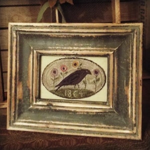 Puede incluir: Una obra de arte de punto de aguja enmarcada que presenta un cuervo negro posado en una rama con flores y el año 1864 bordado en el centro.