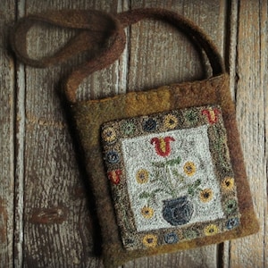Peut inclure: Un petit sac en feutre marron avec une longue bandoulière marron. Le sac est orné d'un patch carré brodé avec un motif floral dans les tons jaunes, rouges, verts et bleus. Le motif représente un vase avec des fleurs et des feuilles.
