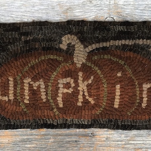 May include: A brown and tan hooked rug with the word "Pumpkin" spelled out in the center of a pumpkin shape.