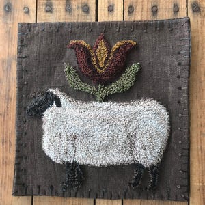 May include: A brown fabric wall hanging with a white sheep and a brown, yellow, and green flower.