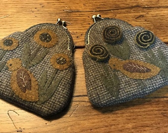 May include: Two brown felt coin purses with different designs. One purse has a floral design with sunflowers and leaves. The other purse has a floral design with brown and green rosettes.