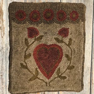 May include: A brown and beige hooked rug with a red heart in the center surrounded by green leaves. The rug has a border of red and brown flowers.