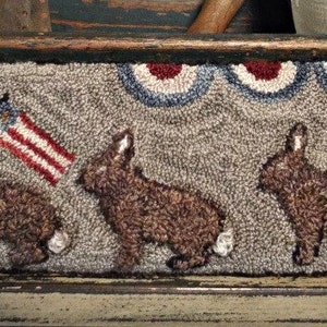 May include: A hand-stitched rug featuring three brown rabbits and a small American flag. The rug has a grey background with a red, white and blue border.