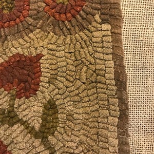 May include: Close-up of a brown and tan hooked rug with a floral design. The rug has a textured surface and is made of wool.