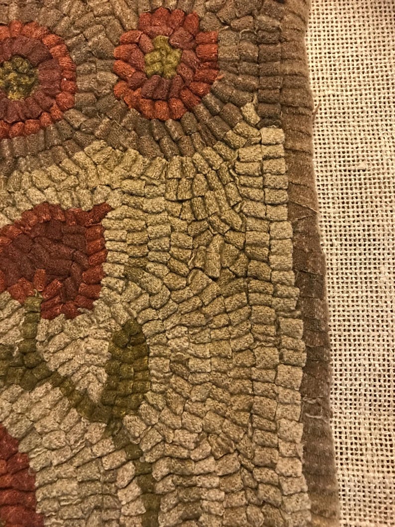 May include: Close-up of a brown and tan hooked rug with a floral design. The rug has a textured surface and is made of wool.