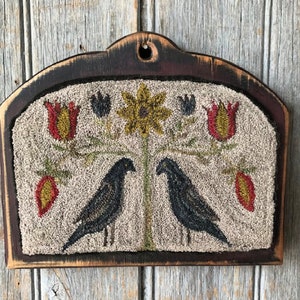 May include: A primitive folk art needlepoint wall hanging featuring two black birds perched on a branch with yellow sunflowers and red tulips. The needlepoint is framed in a dark wood frame with a distressed finish.