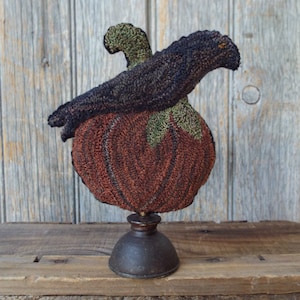 May include: A black crow perched on top of a brown and green pumpkin with a wooden base.