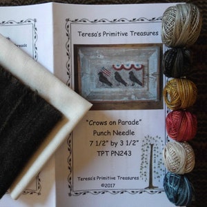 May include: A punch needle kit for a "Crows on Parade" design. The kit includes a piece of beige fabric, a dark brown fabric, and six skeins of embroidery floss in various colours. The kit is 7 1/2 inches by 3 1/2 inches.