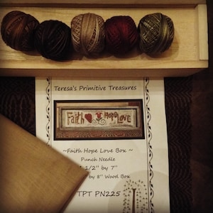 Puede incluir: Un kit de aguja de punzón con hilo de bordar en marrón, beige, rojo y verde. El kit incluye un patrón para una pequeña pieza de bordado que dice "Faith Hope Love" y una caja de madera. El kit está etiquetado como "TPT PN225".