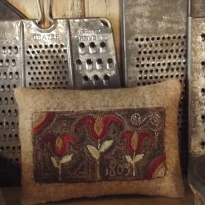 May include: A brown felt pillow with an embroidered design of three stylized red and orange tulips on a brown background. The pillow has the year "1803" embroidered in the bottom right corner.