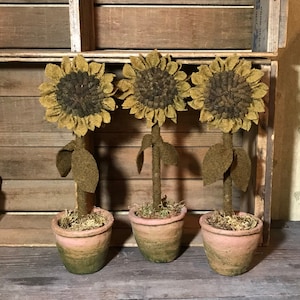 Puede incluir: Tres girasoles de fieltro en macetas de terracota con musgo verde. Los girasoles son marrones y amarillos con hojas verdes.