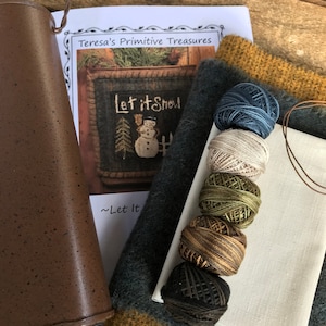 May include: A craft kit for a "Let it Snow" needlepoint project. The kit includes a piece of white linen fabric, a piece of dark blue felt, a piece of brown felt, a piece of gold felt, and six spools of embroidery floss in various colors. The kit also includes a printed pattern with instructions.