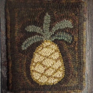 Puede incluir: Alfombra de piña hecha a mano en tonos marrones, verdes y amarillos. La piña está centrada en una alfombra cuadrada con un aspecto texturizado y rústico. La alfombra es de lana y tiene una estética vintage.