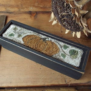 May include: A black wooden box with a needlepoint design of a pumpkin and vines. The box is distressed and has a rustic look.