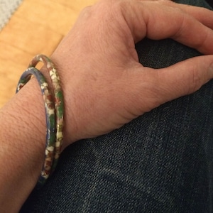 May include: Two colorful bracelets with a blue, green, gold, and red pattern. The bracelets are worn on a person's wrist.