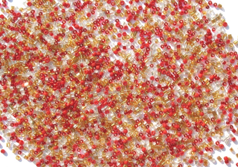 May include: A close-up image of a large quantity of small, round seed beads in red, gold, and clear colors.