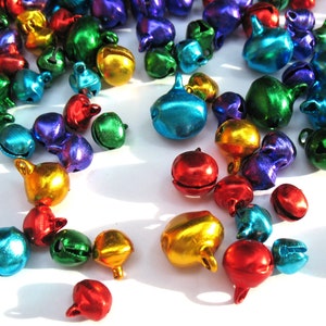 May include: A collection of colourful metal jingle bells in various shades of red, green, blue, gold, and purple. The bells are scattered on a white surface.