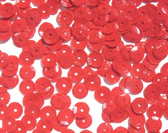 May include: A large quantity of red sequins, scattered on a white background. The sequins are round and have a slightly raised center.
