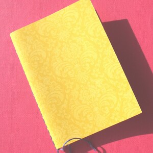May include: A yellow notebook with a black and white damask pattern on the cover. The notebook is closed and has a black thread binding.